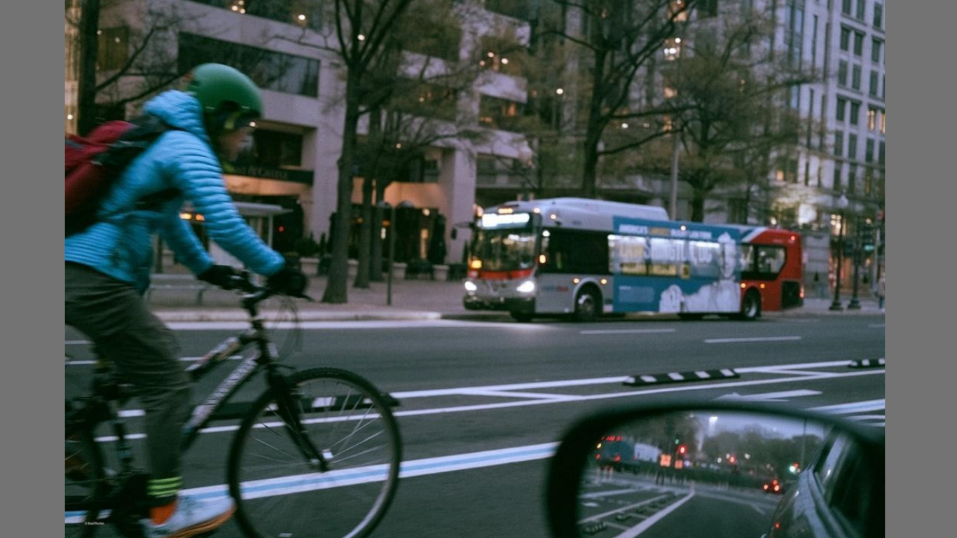 Cyclist and bus on city street at dusk. (Photo by Brad Rucker on Unsplash)